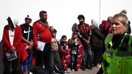 Migrants stand in line as they wait for to be taken for processing in Dungeness, England, August 16, 2023