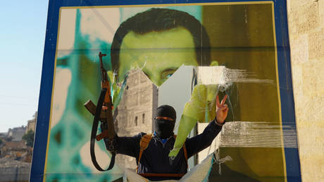 Jihadist militant tearing down a poster of Syrian Presdient Bashar Assad in Aleppo, Syria, November 30, 2024.