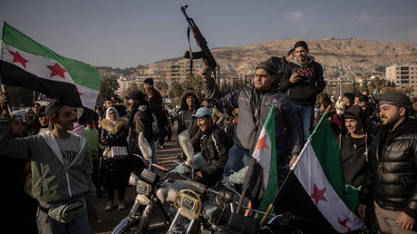 Men pose for a photograph with a gun from a rebel fighter in Umayyad Square on December 20, 2024 in Damascus, Syria.