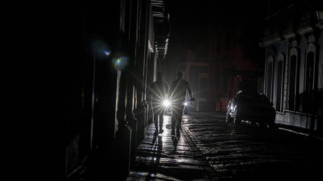 A cars headlights are seen past people walking on a dark in San Juan, Puerto Rico after a major power outage hit the island. © AFP / Ricardo Arduengo