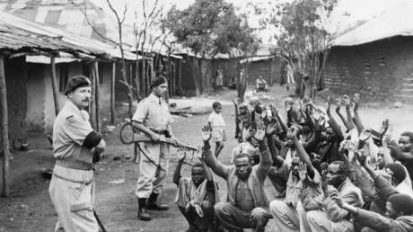 FILE PHOTO. British policemen hold men from the village of Kariobangi at gunpoint while their huts are searched for evidence that they participated in the Mau Mau Rebellion of 1952.