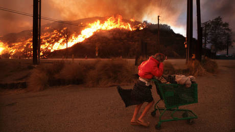 A homeless woman pushes her belongings off Pacific Coast Highway and Topanga Canyon Blvd, Pacific Palisades, California, January 7, 2025.