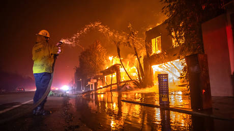 A firefighter battles the Palisades Fire while it burns homes at Pacific Coast Highway amid a powerful windstorm on January 8, 2025 in Los Angeles, California.