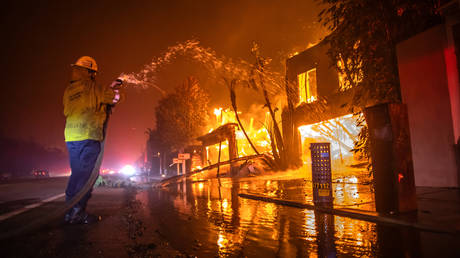 A firefighter battles the Palisades Fire while it burns homes at Pacific Coast Highway amid a powerful windstorm on January 8, 2025 in Los Angeles, California.